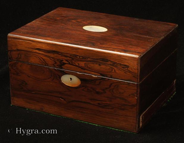 Antique Figured Rosewood box with lift-out compartmentalized tray and sprung drawer fitted for jewelry. There are mother of pearl escutcheons to the top and the front. There is a ruched velvet pad in the lid is framed with gold embossed leather behind. It is released by pressing behind the lock catch. The sprung drawer is released by removing a brass pin. The lift-out tray is of mahogany construction with rosewood facings. New pads of velvet have been made to make the tray suitable for jewelry. There is further space beneath. Circa 1840. - Enlarge Picture